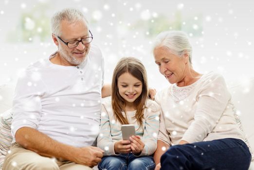 family, generation, technology and people concept - smiling grandfather, granddaughter and grandmother with smartphone sitting on couch at home