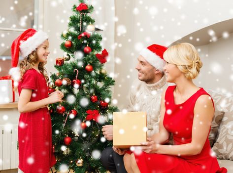 christmas, holidays, happiness and people concept - smiling family in santa helper hats with gift box at home