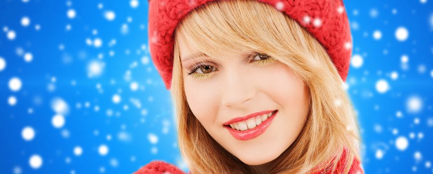 happiness, winter holidays, christmas and people concept - close up of smiling young woman in red hat and scarf over blue snowy background