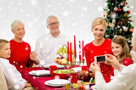 family, holidays, generation, christmas and people concept - smiling family having dinner and taking photo with camera at home