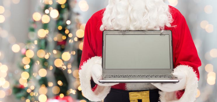christmas, advertisement, technology, and people concept - close up of santa claus with laptop computer over tree lights background