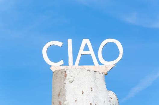 Ciao lettering on an old tree trunk in front of blue sky.