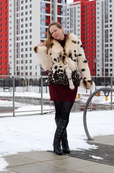 The woman in a fur coat costs against new buildings.