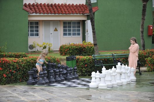 Girls in towels are playing chess with big figures.