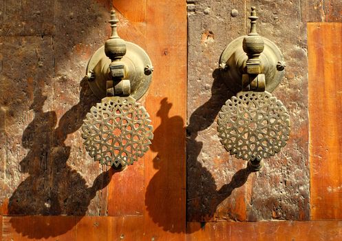 Decorated ornamental bronze door knobs the gates of moroccan palace in evening sun