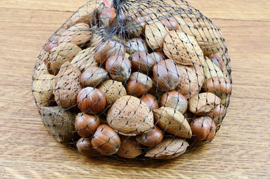 Mixed nuts on wooden background in net sack

