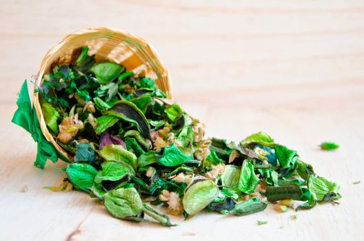 Fragrant natural potpourri with dried flowers, leaves and spices spilling out of a rectangular weave basket onto a wooden background for that special fragrance in the house