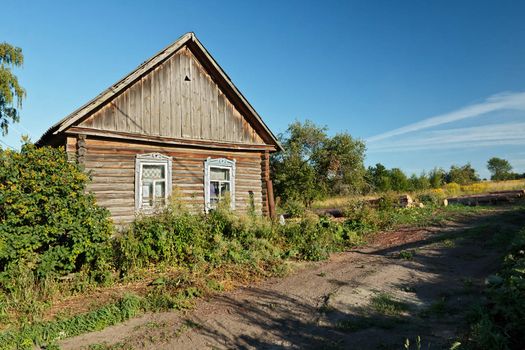 Timber house in Russian countryside near unsurfaced road in summer late afternoon