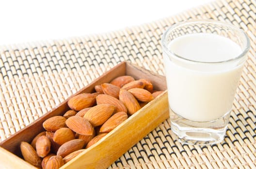 Almond milk in glass with almonds on wooden mat