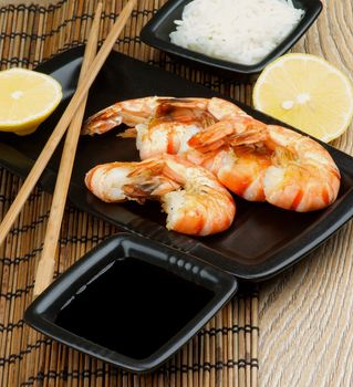 Delicious Asian Style Roasted Shrimps with Soy Sauce, Boiled Rice, Lemon and Chopsticks on Straw Mat background closeup