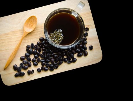 Black coffee in glass cup and seed coffee on wooden background.