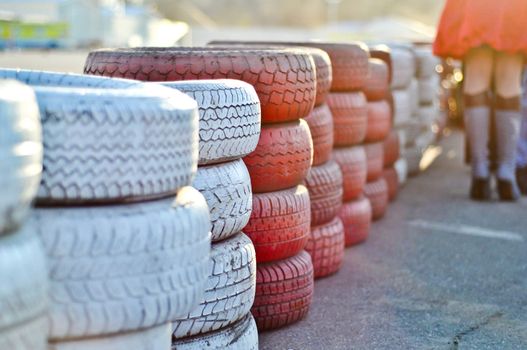 racetrack fence of white and red of old tires and female legs in boots