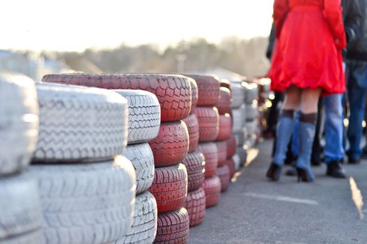 racetrack fence of white and red of old tires and female legs in boots