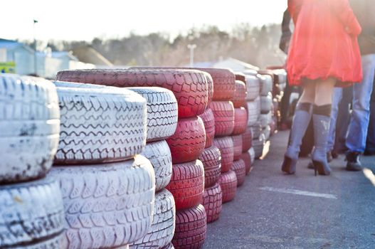 racetrack fence of white and red of old tires and female legs in boots