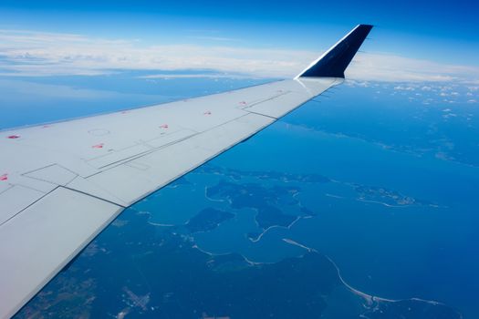 Wing of an airplane flying above a coastal region. 