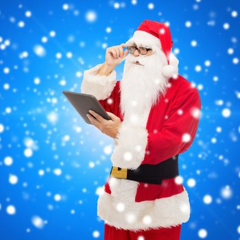 christmas, holidays, technology and people concept - man in costume of santa claus with tablet pc computer over blue snowy background