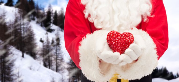 christmas, holidays, love, charity and people concept - close up of santa claus with heart shape decoration over snowy mountains