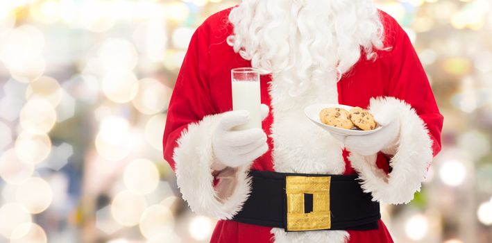 christmas, holidays, food, drink and people concept -close up of santa claus with glass of milk and cookies over lights background