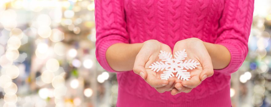 christmas, holidays and people concept - close up of woman in pink sweater holding snowflake over lights background