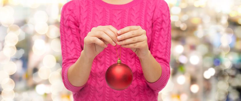 christmas, decoration, holidays and people concept - close up of woman in pink sweater holding christmas ball over lights background