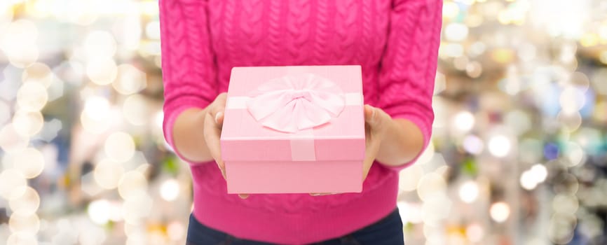 christmas, holidays and people concept - close up of woman in pink sweater holding gift box over lights background