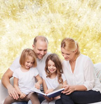 family, childhood, holidays and people - smiling mother, father and little girls reading book over yellow lights background