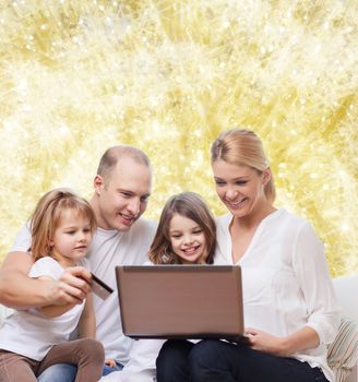 family, holidays, shopping, technology and people - happy family with laptop computer and credit card over yellow lights background