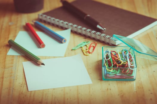 Notebook and sticky paper, paper clip, color pencil, and pen on wood table with vintage filter effect