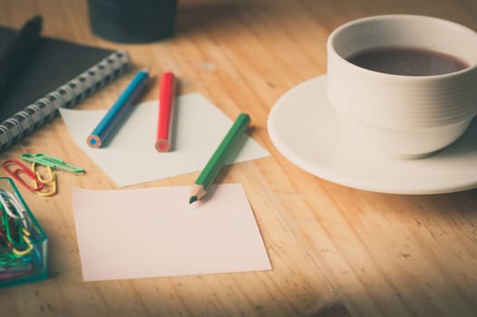 Notebook and sticky paper, paper clip, color pencil, and pen on wood table with vintage filter effect