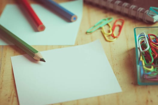 Notebook and sticky paper, paper clip, color pencil, and pen on wood table with vintage filter effect