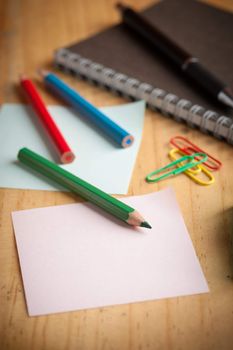 Notebook and sticky paper, paper clip, color pencil, and pen on wood table