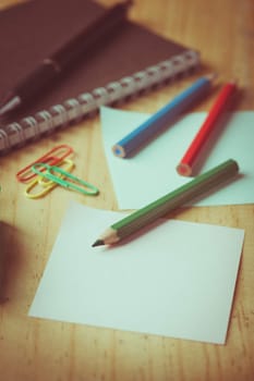 Notebook and sticky paper, paper clip, color pencil, and pen on wood table with vintage filter effect