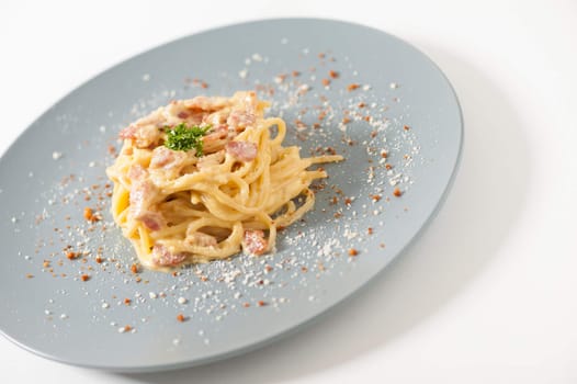 Carbonara pasta with bacon in grey ceramic dish.