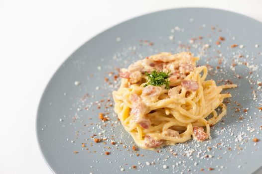 Carbonara pasta with bacon in grey ceramic dish.
