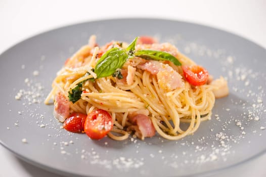 Pasta with bacon and tomato in grey ceramic dish.