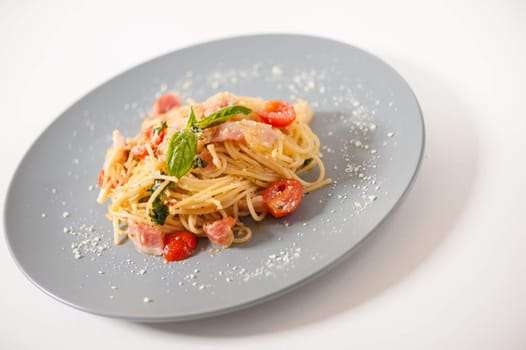 Pasta with bacon and tomato in grey ceramic dish.