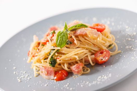 Pasta with bacon and tomato in grey ceramic dish.