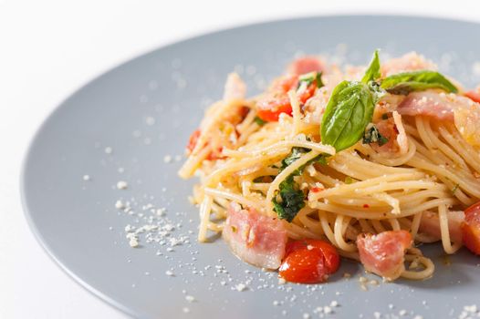 Pasta with bacon and tomato in grey ceramic dish.