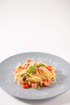 Pasta with bacon and tomato in grey ceramic dish.