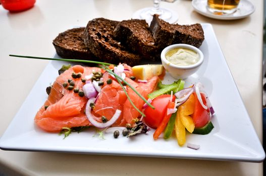 a dish of red salted fish with brown bread on a white square plate