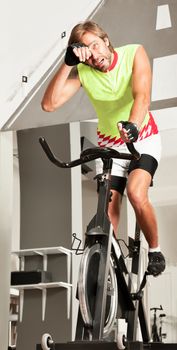 Young attractive tired male is working out in a spinning bike gym.