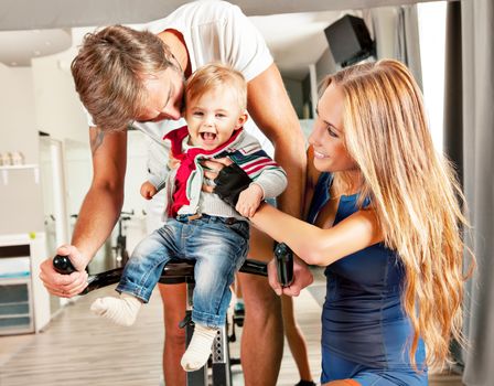 Young beautiful mother and father having fun embracing their cute little boy with affection in a cycling gym.