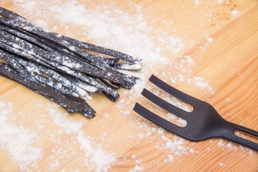 still life: black pasta, flour,  fork on wood table