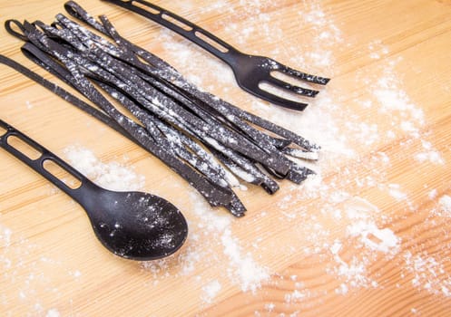 still life: black pasta, flour, spoon, fork on wood table