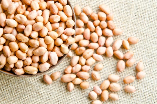Raw peanuts or arachis in wooden cup on sack background.