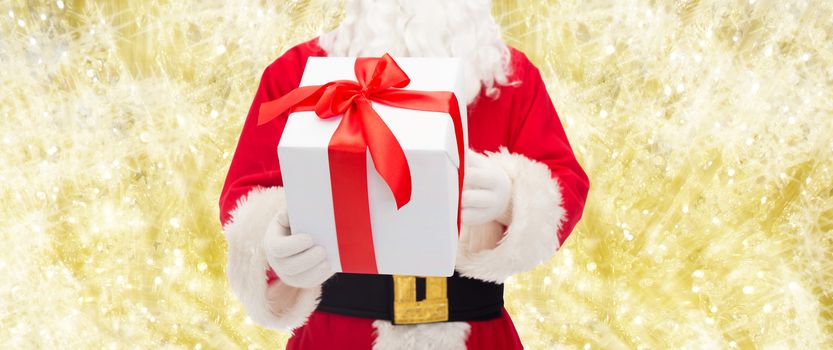 christmas, holidays and people concept - close up of santa claus with gift box over yellow lights background