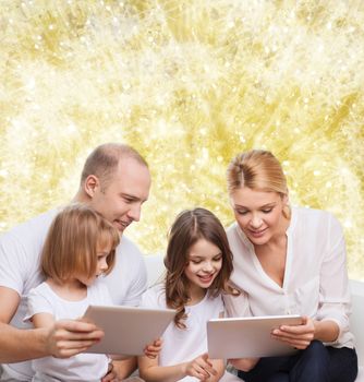family, holidays, technology and people - smiling mother, father and little girls with tablet pc computers over yellow lights background
