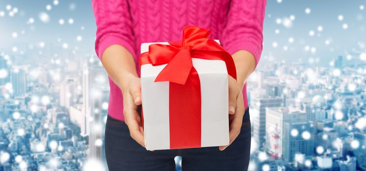 christmas, holidays and people concept - close up of woman in pink sweater holding gift box over snowy city background
