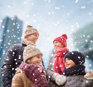 family, childhood, season and people concept - happy family in winter clothes over snowy city background