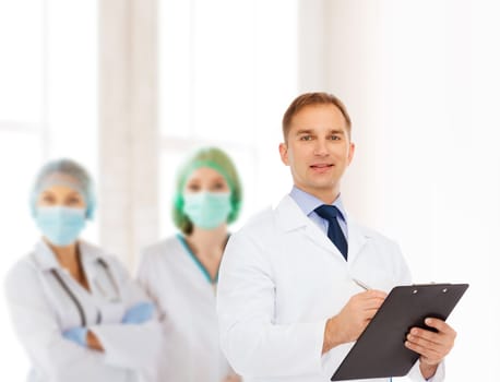 medicine, profession, teamwork and healthcare concept - smiling male doctor with clipboard writing prescription over group of medics